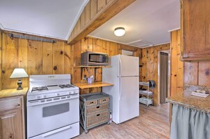Cocina compacta con estufa, microondas y refrigerador, paredes de madera y una pequeña encimera.