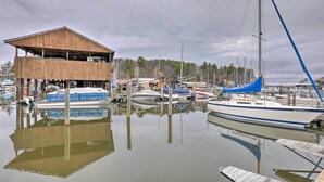 En lystbådehavn med både fortøjet ved træbrygger, en træbygning med skråt tag og en klar himmel.