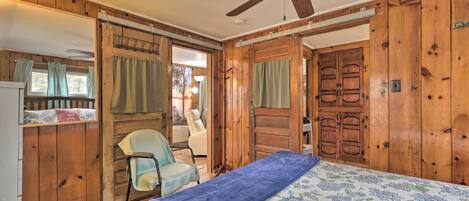 A wooden cabin bedroom with a bed, a chair, and a ceiling fan.
