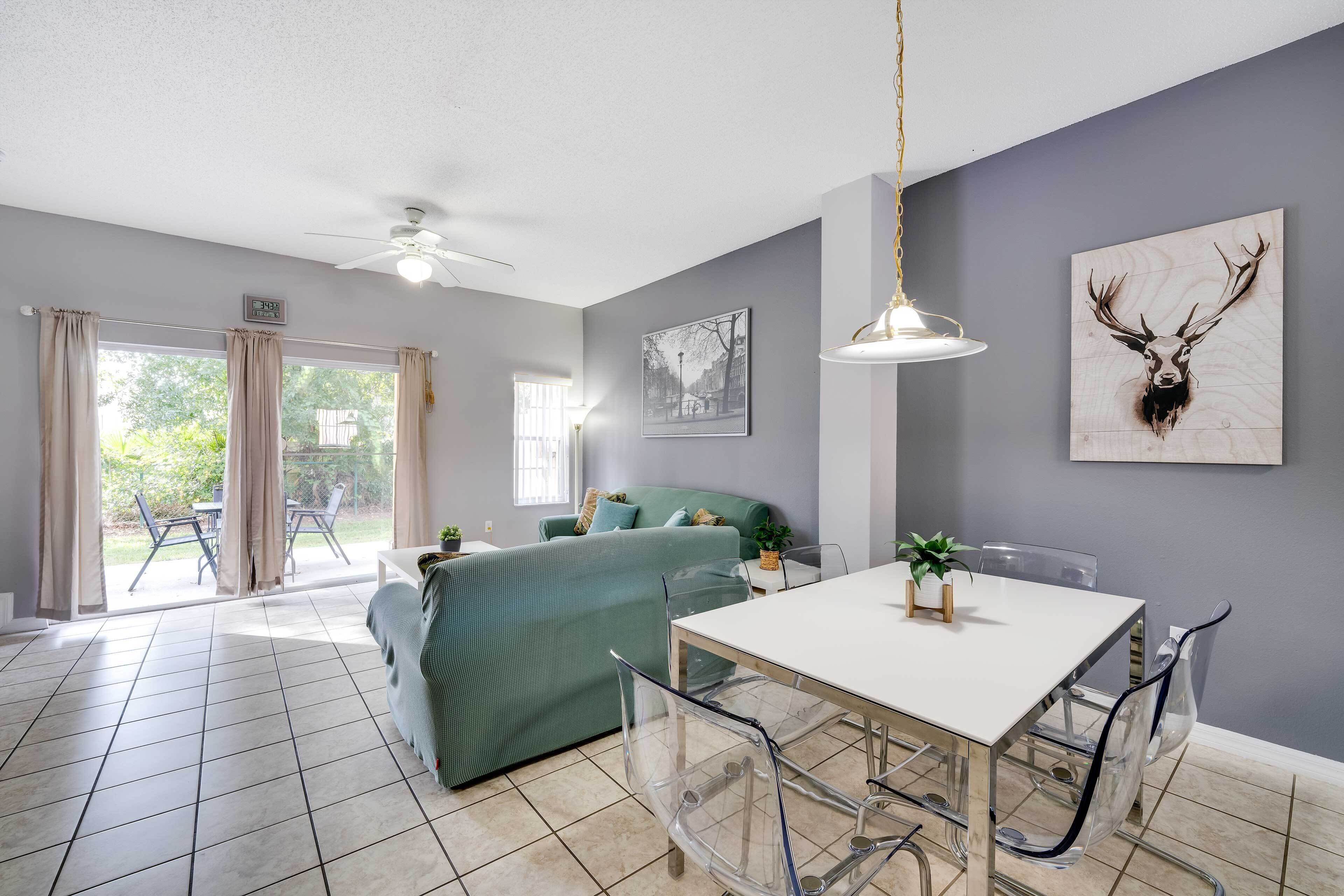 Un soggiorno moderno con un divano verde, un tavolo da pranzo con sedie, una ventola a soffitto e un'ampia finestra con tende.