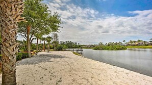 A sandy beach area with a palm tree, a bridge, and a calm lake. - Kissimmee Escape ~ 10 Mi to Disney World! (Kissimmee)