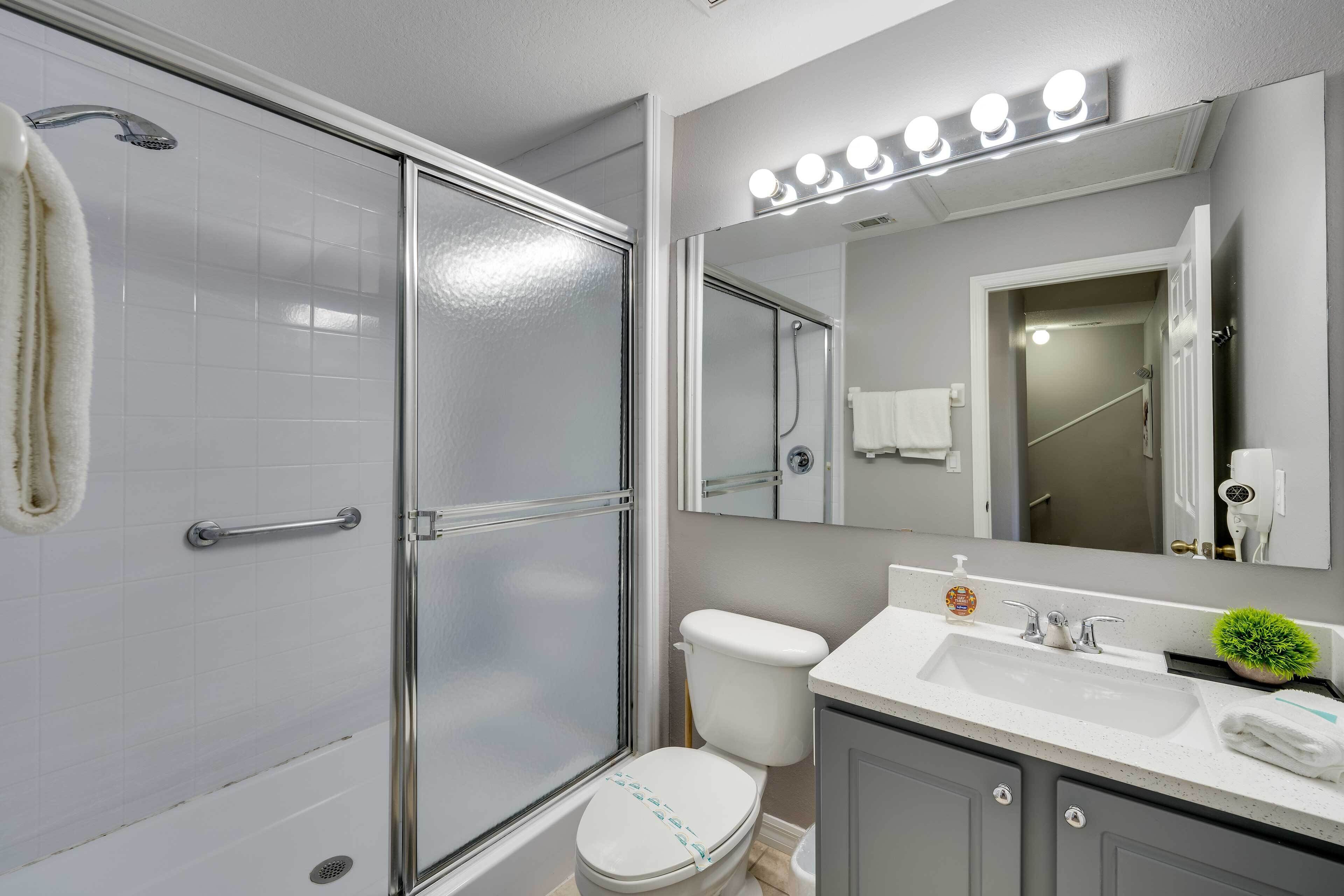 A modern bathroom with a glass shower enclosure, a white toilet, a vanity with a sink, and a mirror with lights above.