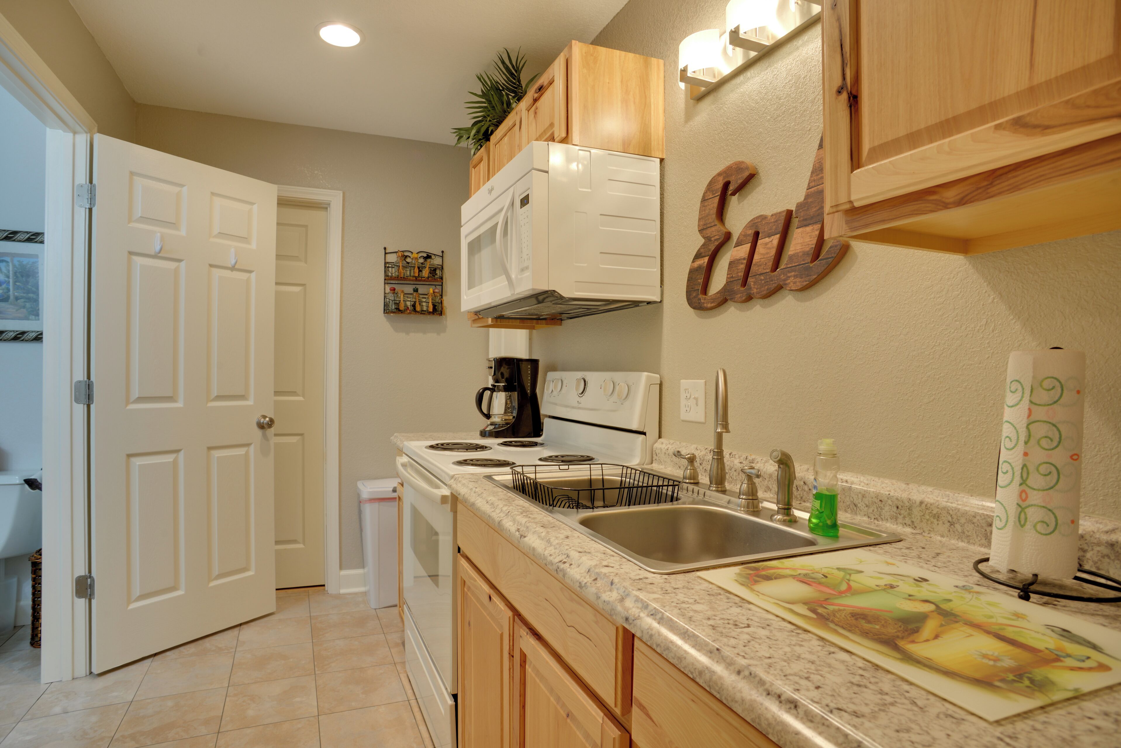 A kitchen with wooden cabinets, a microwave, a stove, a sink, and a coffee maker.