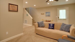 A living room with a beige sofa, two patterned pillows, a ceiling fan, and a staircase leading to another level. - Wooded Gilbertsville Hideaway on Kentucky Lake! (Gilbertsville)