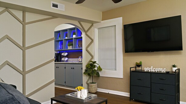 A living room with a sofa, a coffee table with a tray, a TV, a cabinet, and a kitchen area with blue lighting. - Rare Find Downtown Florence 2 Br (Florence)