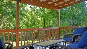 A covered outdoor seating area with wicker furniture and a glass table, surrounded by a wooden deck and lush greenery. - Rare Find Downtown Florence 2 Br (Florence)