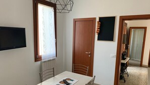 Een eethoek met een witte tafel, twee stoelen, een raam met gordijn, een deur en een prikbord aan de muur.
