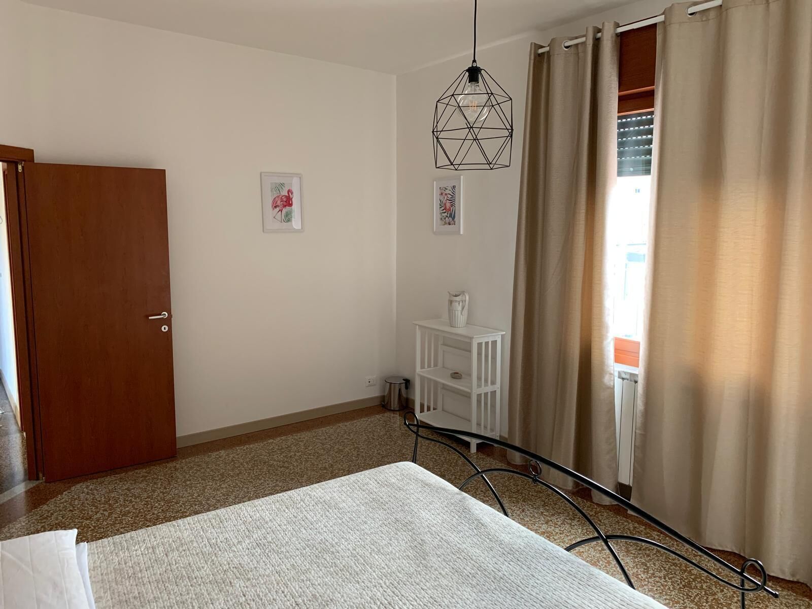 A hotel room with a bed, a desk with a lamp, a door, and a window with curtains.