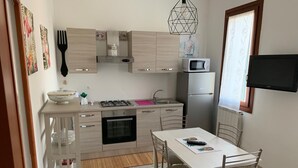 Een compacte keuken met een gasfornuis, oven, magnetron en een klein spoelbakje. Er is een eettafel met stoelen en een tv aan de muur bevestigd.