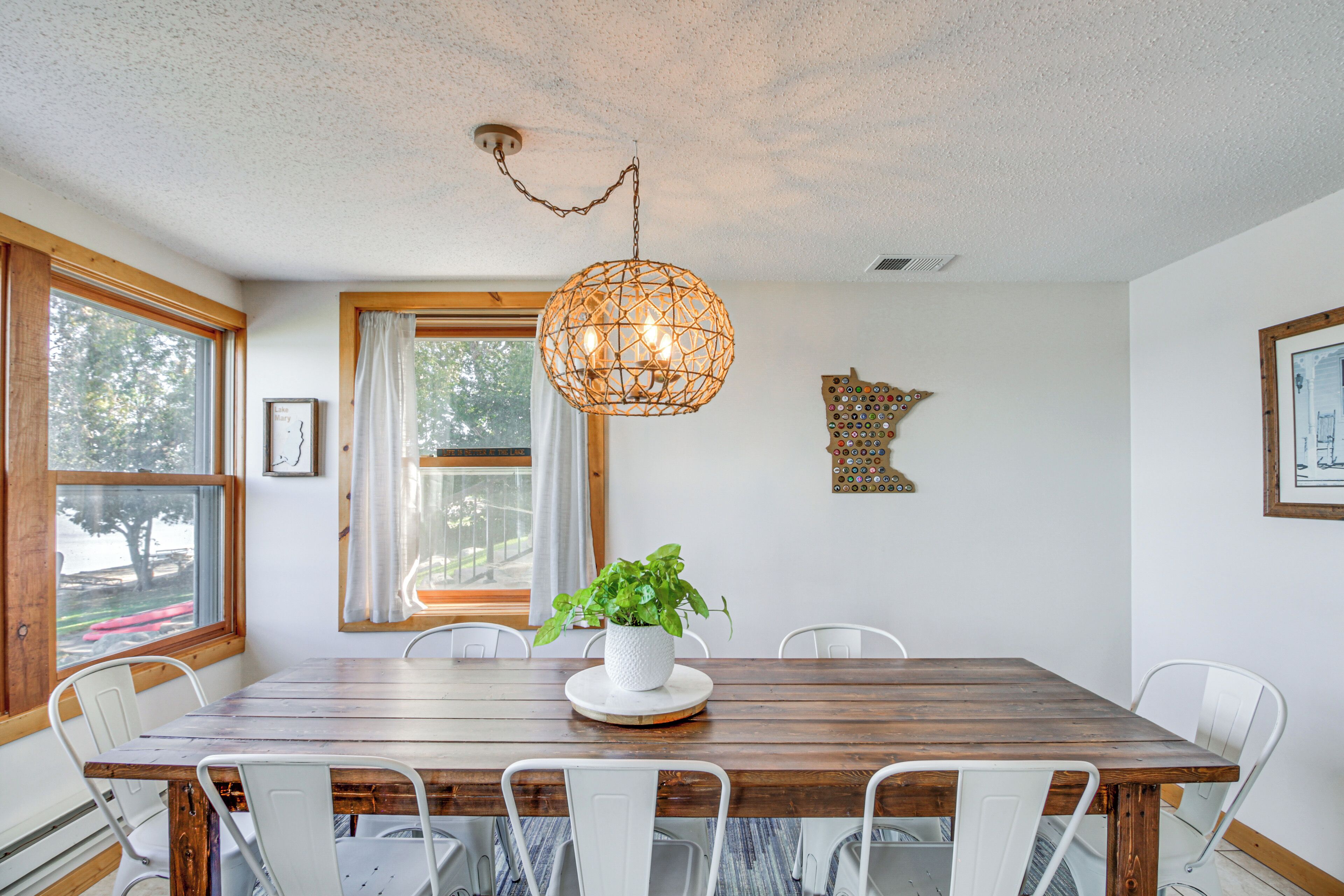 Un coin repas avec une table en bois, des chaises blanches, un luminaire suspendu et une plante en pot.