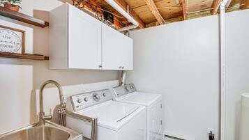 A laundry room with a stainless steel sink, a washing machine, and a dryer. There are wooden beams on the ceiling and a white cabinet above the washing machine.