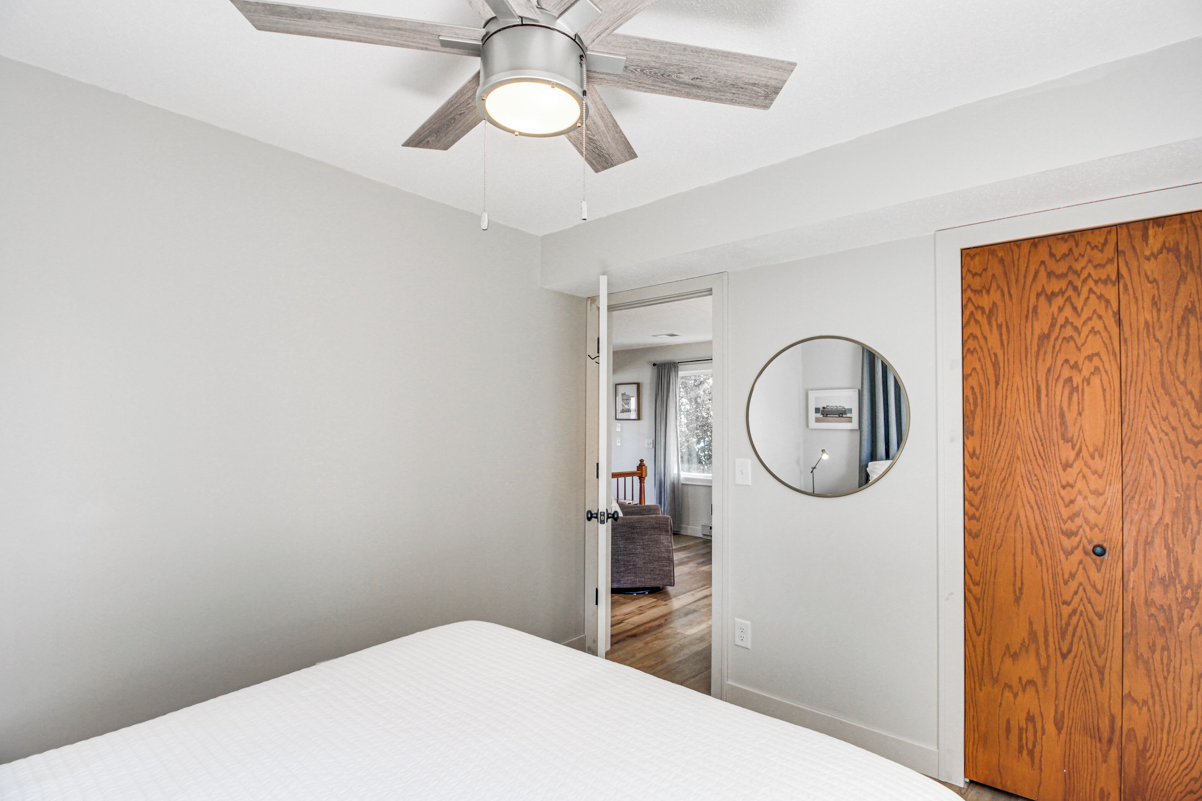 A bedroom with a bed, a ceiling fan, a wooden door, and a hallway leading to another room.