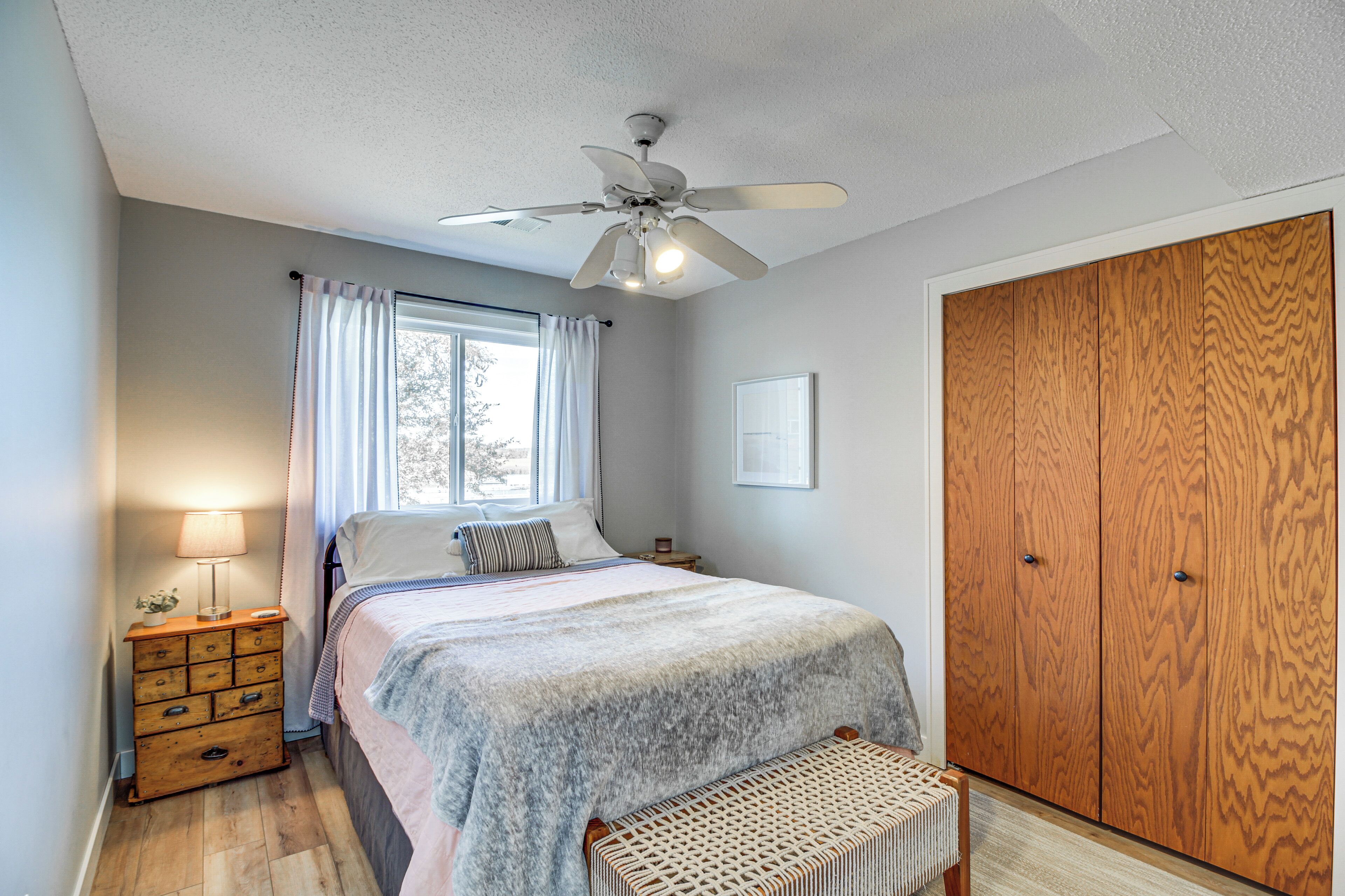 A bedroom with a bed, a wooden wardrobe, a nightstand with a lamp, and a window with curtains.