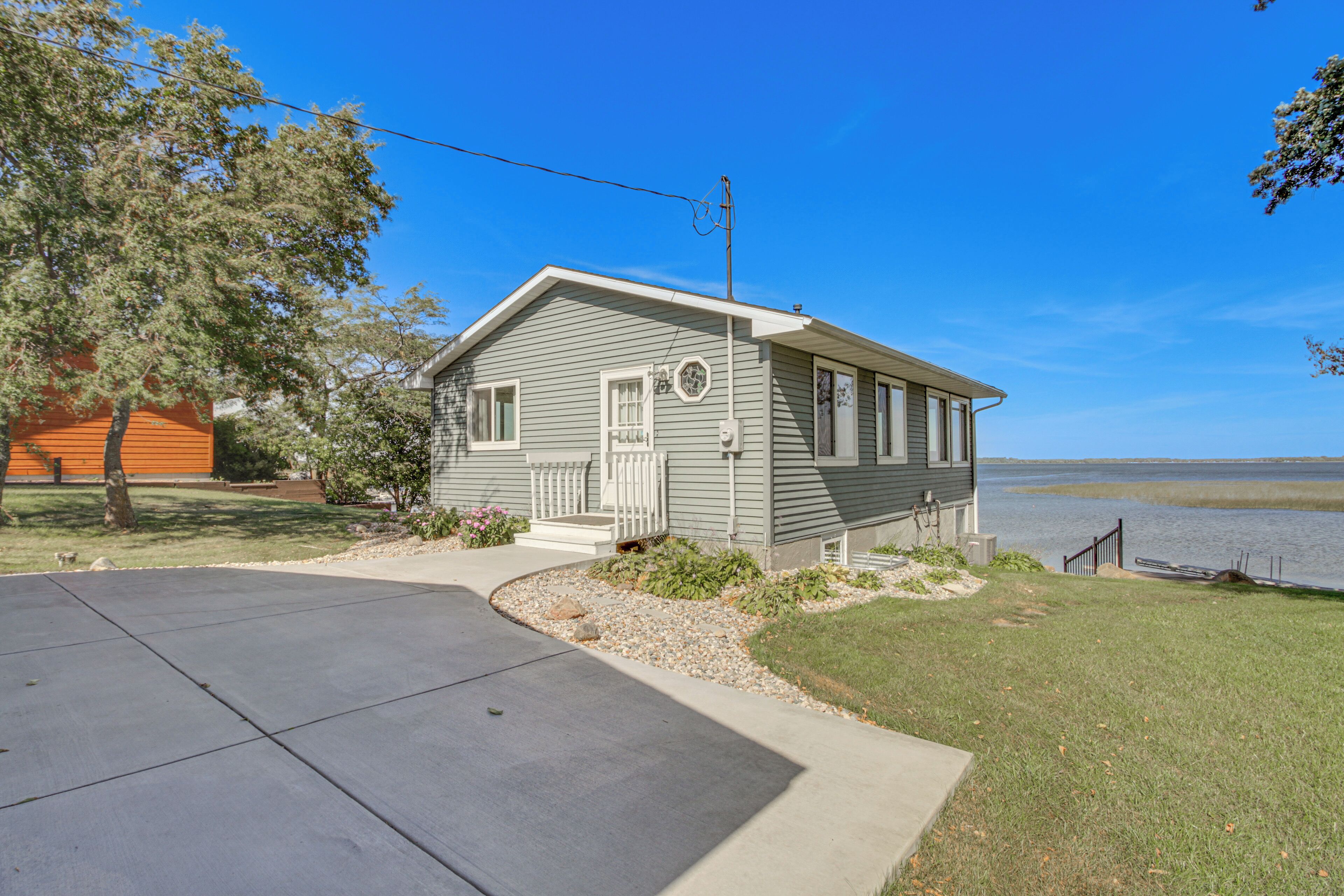 A single-story house with a front porch, a small deck, and a view of a body of water.