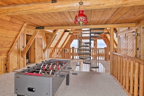 A wooden-floored room with a foosball table and a spiral staircase.