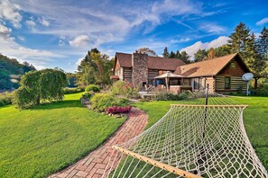 Une cabane en rondins avec une cheminée en pierre, un hamac et un chemin de briques menant à l’entrée.