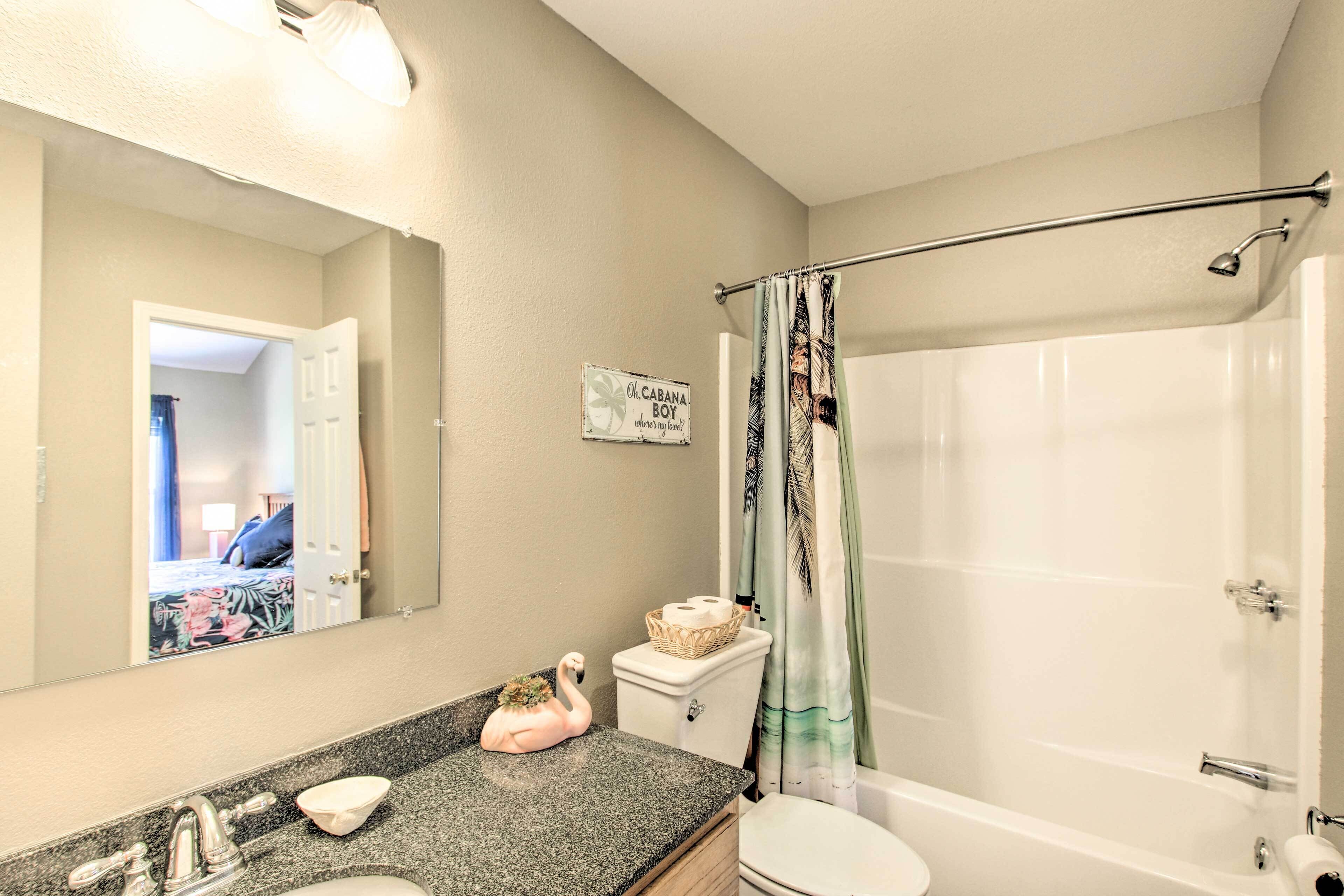 A bathroom with a sink, toilet, and shower. There is a sign on the wall and a decorative swan on the counter.