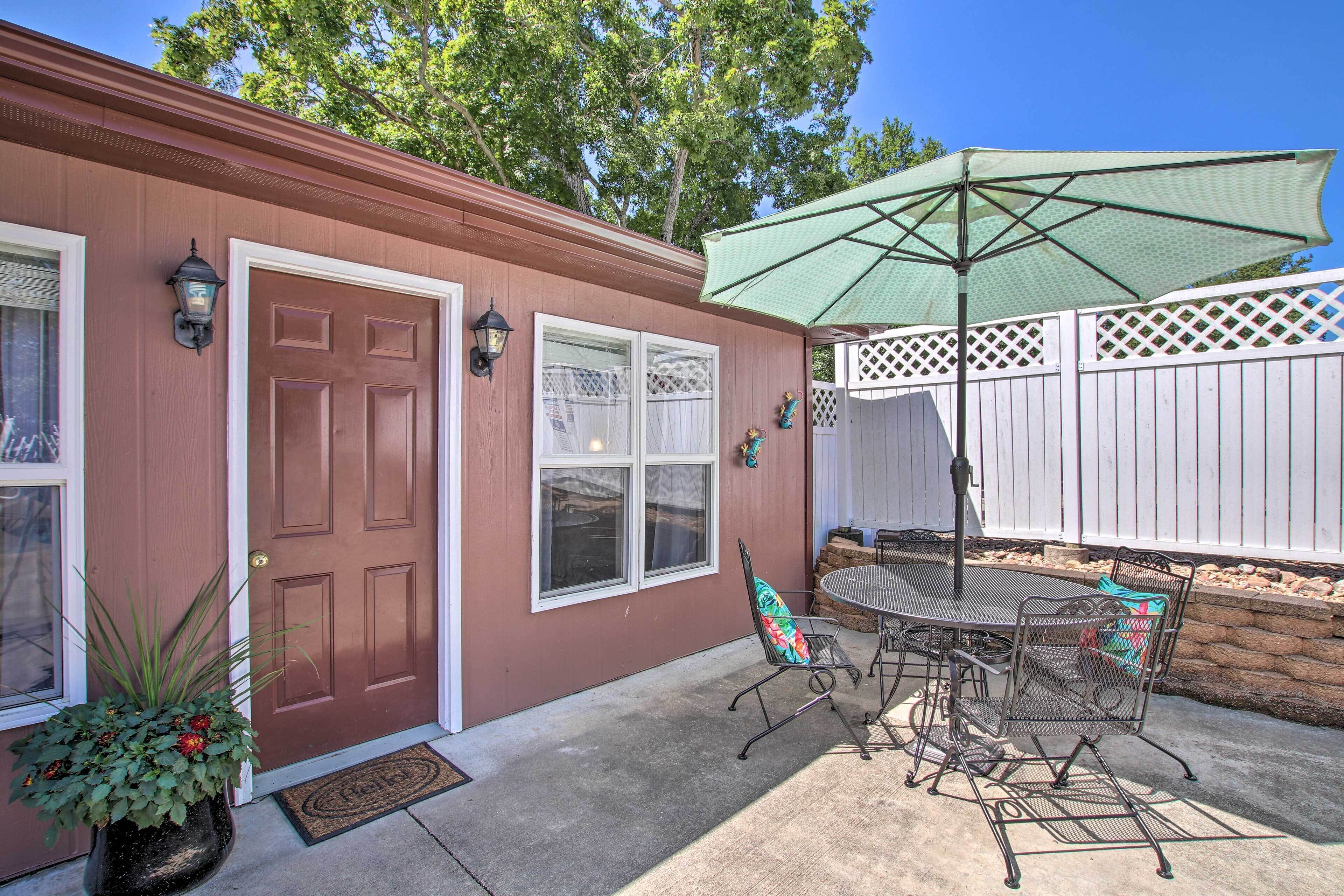 A patio with a table and chairs, a green umbrella, and a white fence.