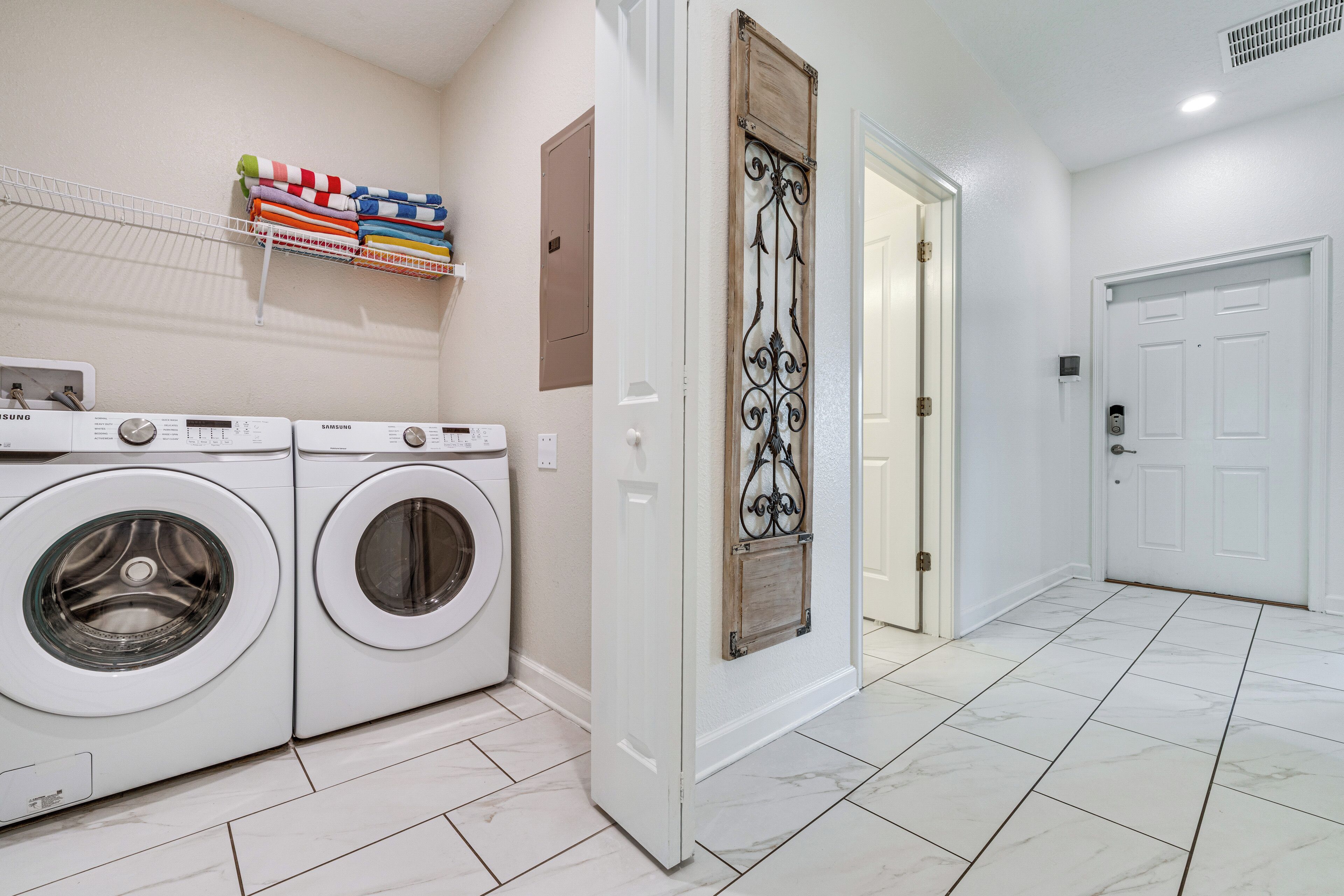 A laundry room with two white front-loading washing machines, a shelf with folded towels, and a decorative iron gate.