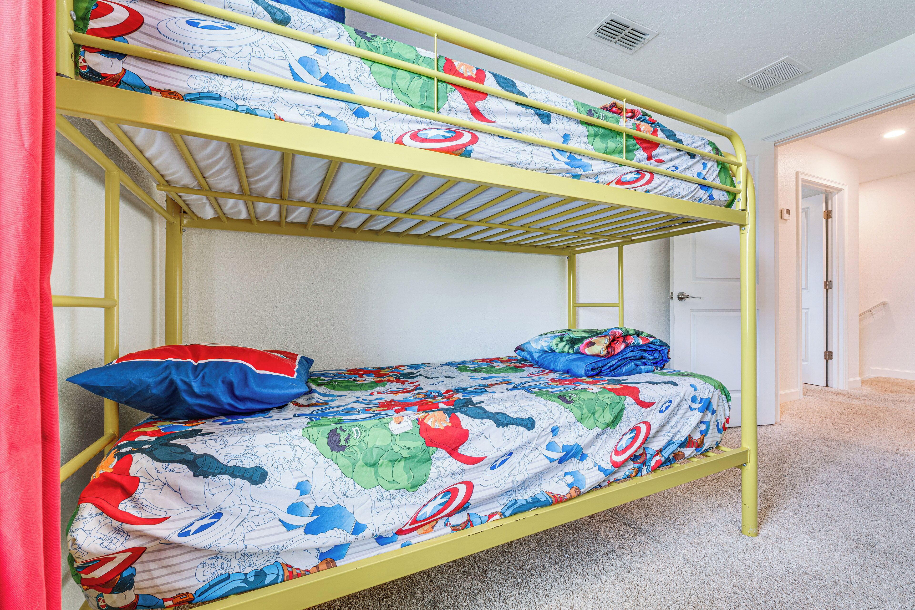 A bunk bed with superhero-themed bedding in a room with white walls and carpet.