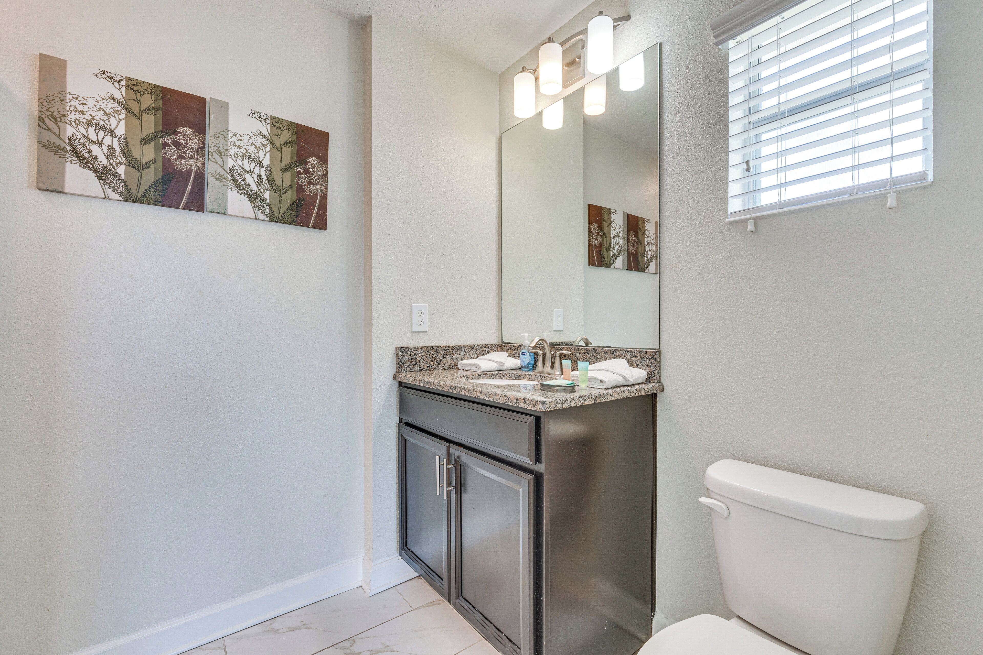A bathroom with a toilet, sink, cabinet, and a mirror with lights.