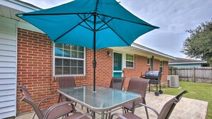 An outdoor patio with a glass table and metal chairs, a blue umbrella, and a barbecue grill. - Breezy Gulfport Getaway < 1 Mile to Beach + Casino (Gulfport)