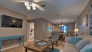 A spacious living room with a ceiling fan, a television mounted on the wall, a dining area with a table and chairs, and a cozy seating area with a sofa and cushions. - Breezy Gulfport Getaway < 1 Mile to Beach + Casino (Gulfport)