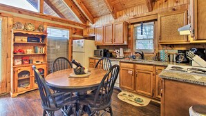 A wooden cabin interior with a dining table, chairs, a kitchen area with appliances, and a chandelier. - Sevierville Cabin w/ Private Hot Tub & Fireplace! (Sevierville)