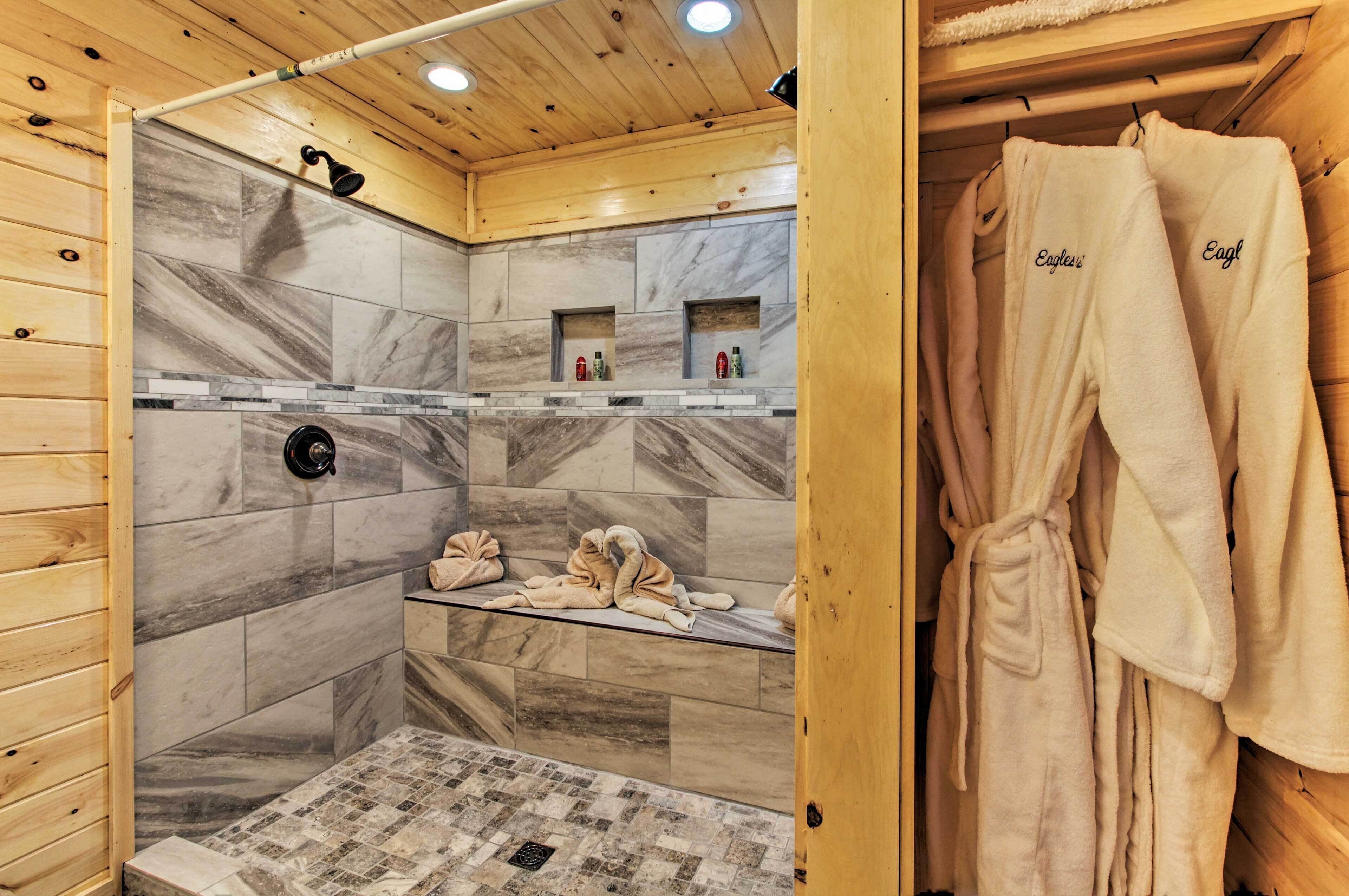 Een houten badkamer in een chalet, met een douche, marmeren tegels en een glazen plank met handdoeken.