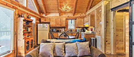 A cozy cabin interior with a wooden ceiling, a dining area, and a sofa with cushions.