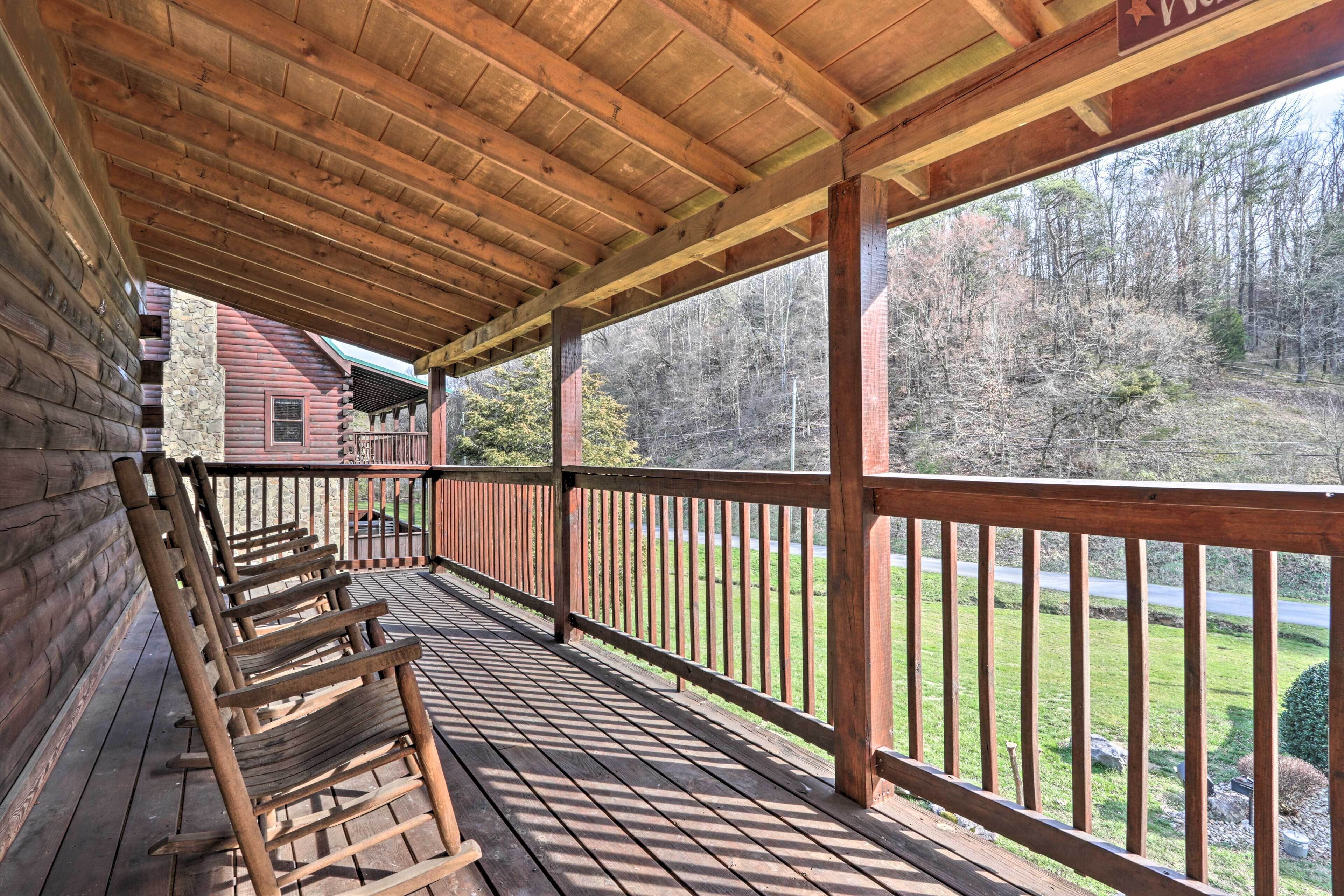 A wooden deck with rocking chairs, a stone wall, and a view of a forested area.