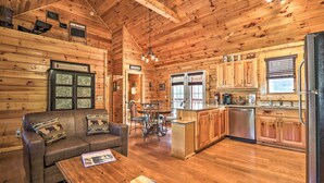 A cabin interior with a wooden interior, a sofa, a dining table, and a kitchen area with wooden cabinets and a refrigerator. - 3 Mi to Dollywood: Hot Tub Hideaway in Smoky Mtns (Sevierville)