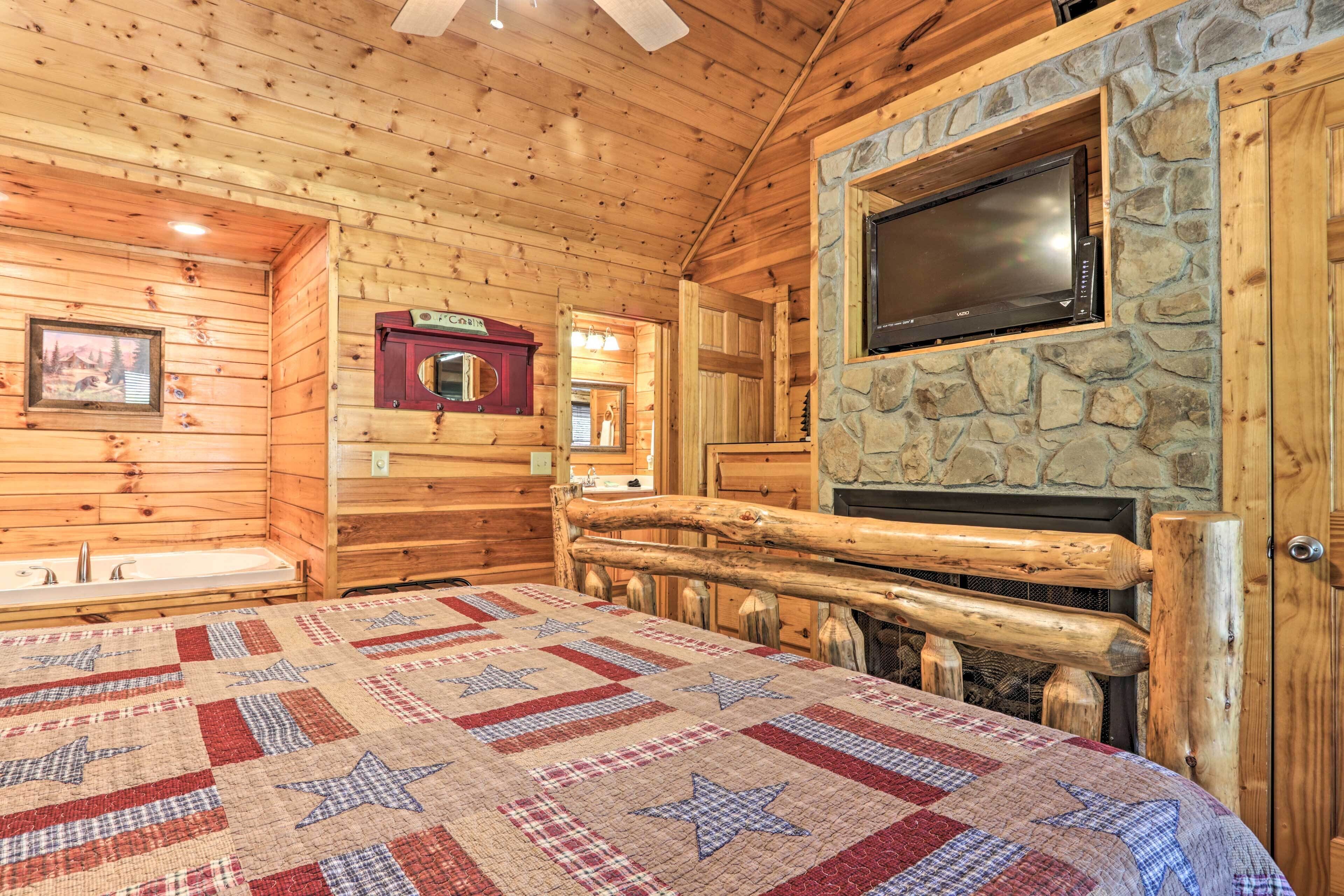 Habitación de cabaña de troncos con una cama, una chimenea de piedra, un televisor montado en la pared y un banco de madera.