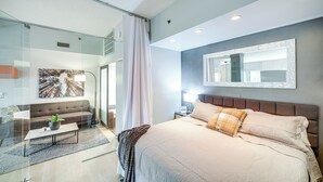 A modern bedroom with a large bed, a glass partition, a sofa, and a mirror on the wall. - Dtwn Cleveland Loft-style Condo: Walk to Stadiums! (Cleveland)