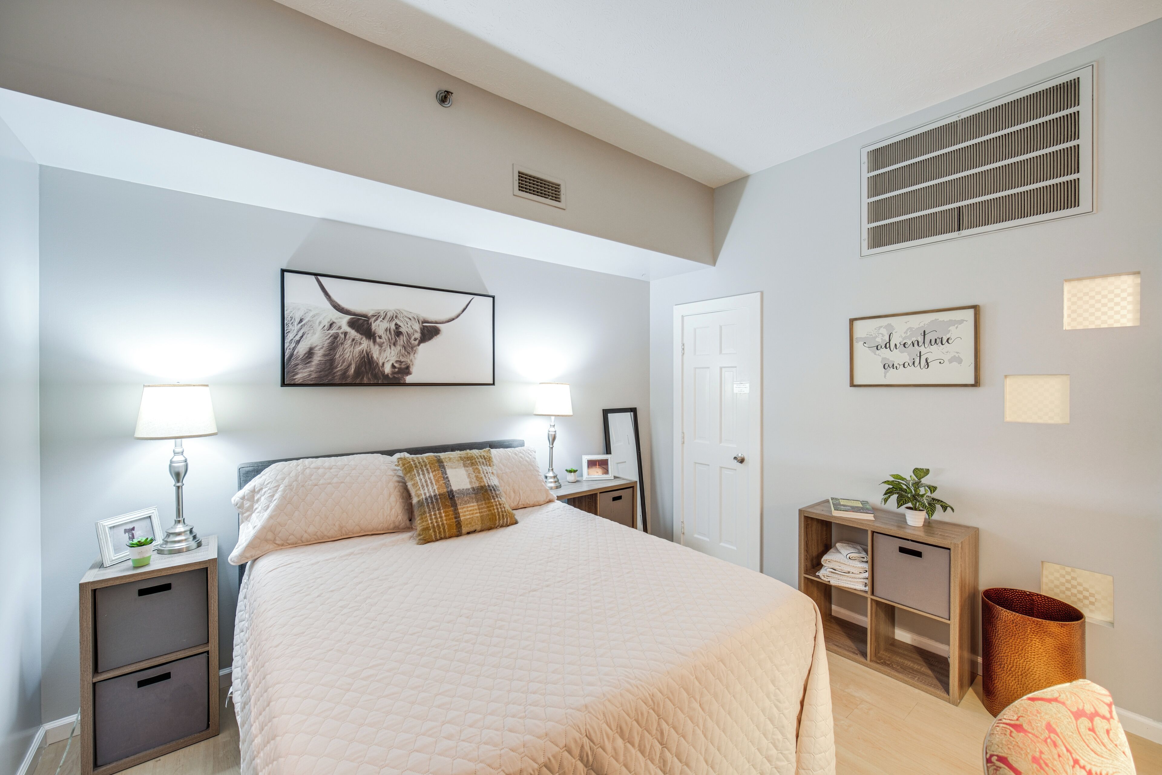 A bedroom with a large bed, bedside tables, a nightstand, a wall-mounted shelf, and a door.