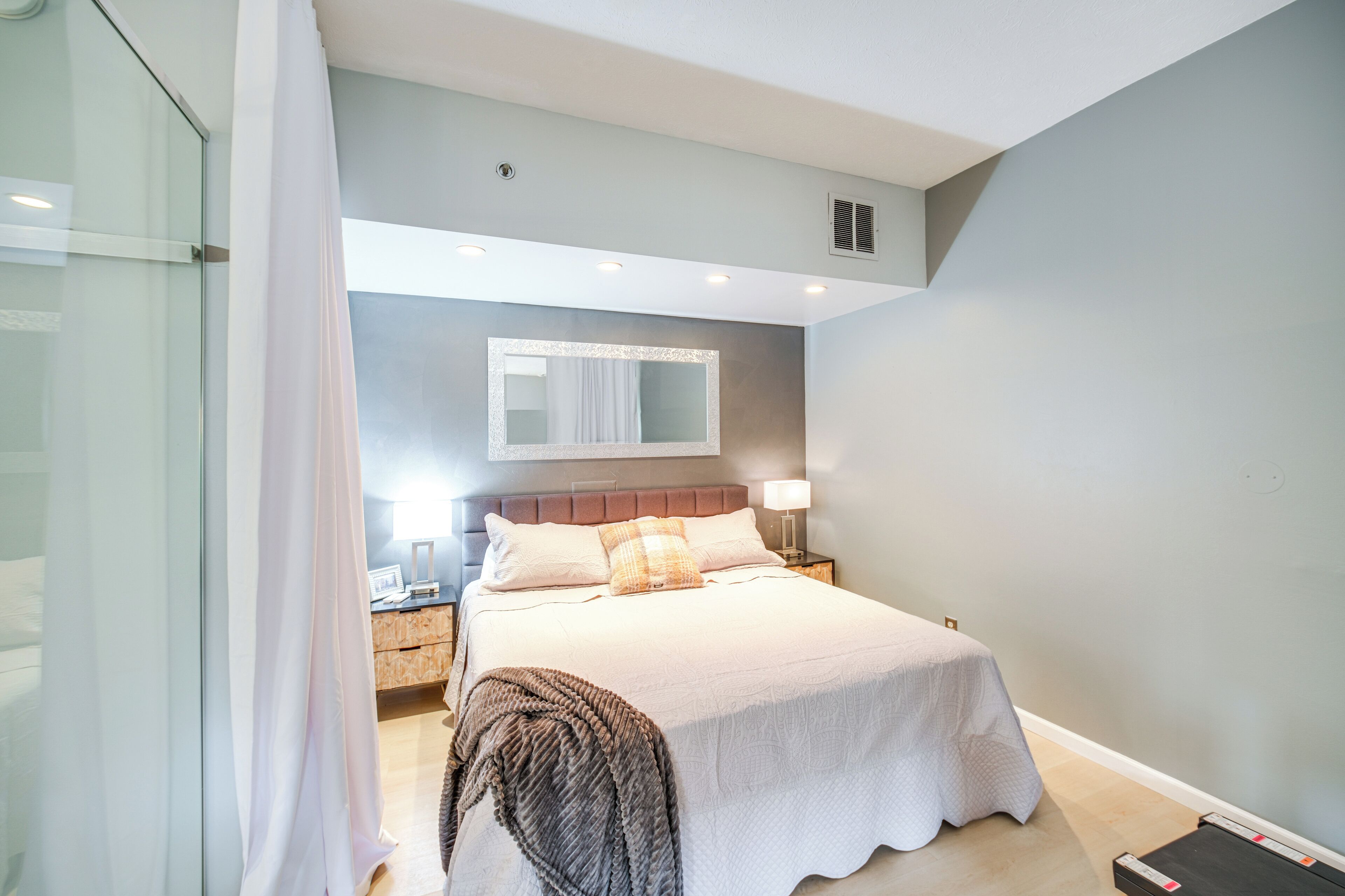 Une chambre à coucher moderne avec un grand lit, une table de chevet avec une lampe et un miroir au-dessus du lit.
