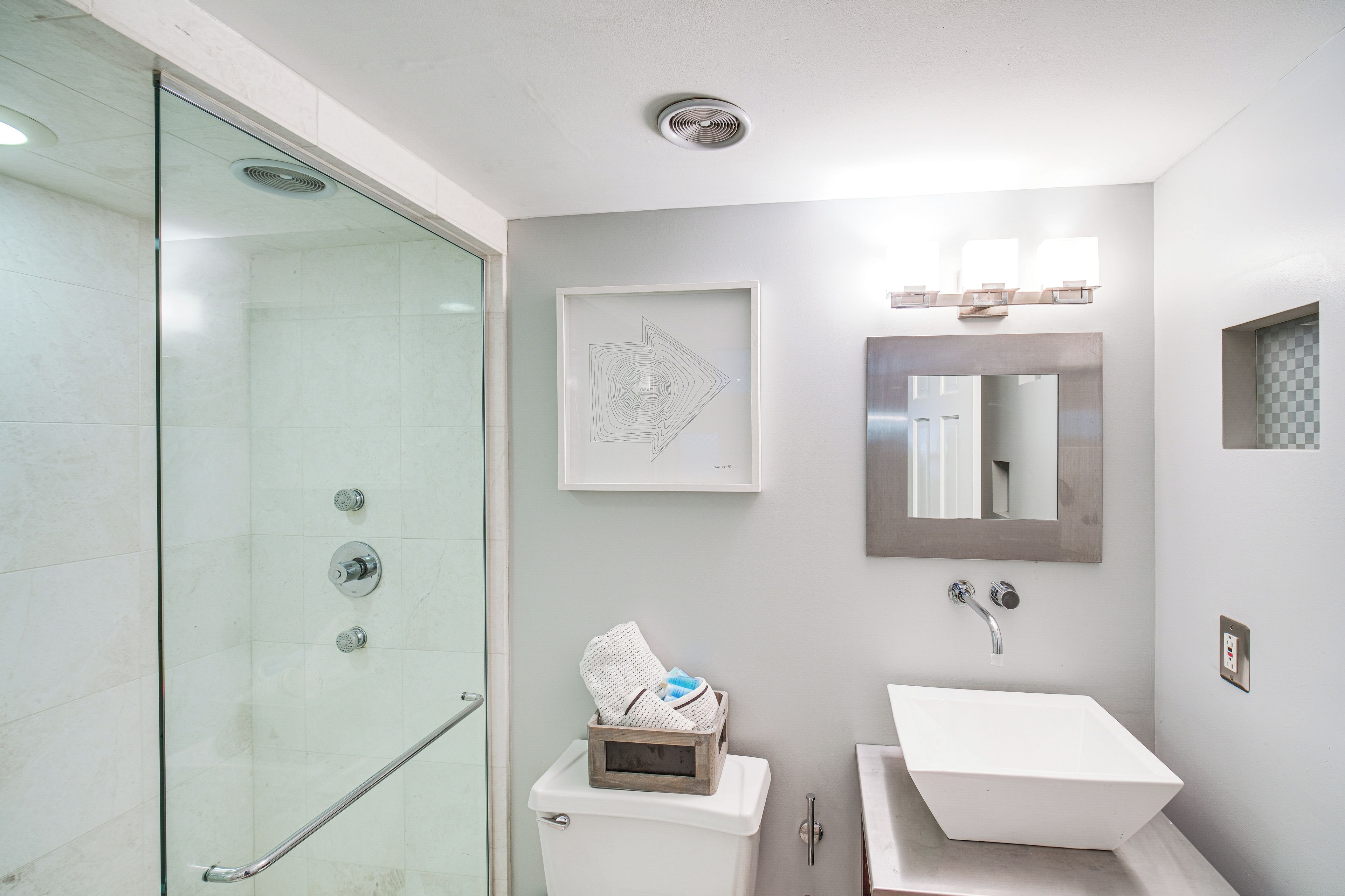 A modern bathroom with a glass shower enclosure, a white sink, and a framed artwork on the wall.