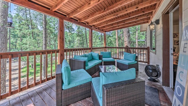 A covered outdoor seating area with wicker furniture and teal cushions, overlooking a forested area. - Pet-friendly Ruidoso Home w/ Deck & Forest Views! (Ruidoso)