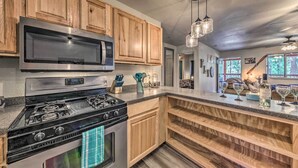 A kitchen with wooden cabinets, a stainless steel microwave, a gas stove, and a built-in oven. There are hanging lights and a wine rack with glasses. - Pet-friendly Ruidoso Home w/ Deck & Forest Views! (Ruidoso)