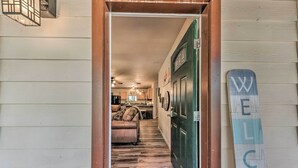 A wooden interior hallway with a green door, a welcome sign, and a kitchen area in the background. - Pet-friendly Ruidoso Home w/ Deck & Forest Views! (Ruidoso)