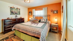 Ein Schlafzimmer mit einem großen Bett, einem Schminktisch, einem Nachttisch und einem Fenster mit Vorhängen.