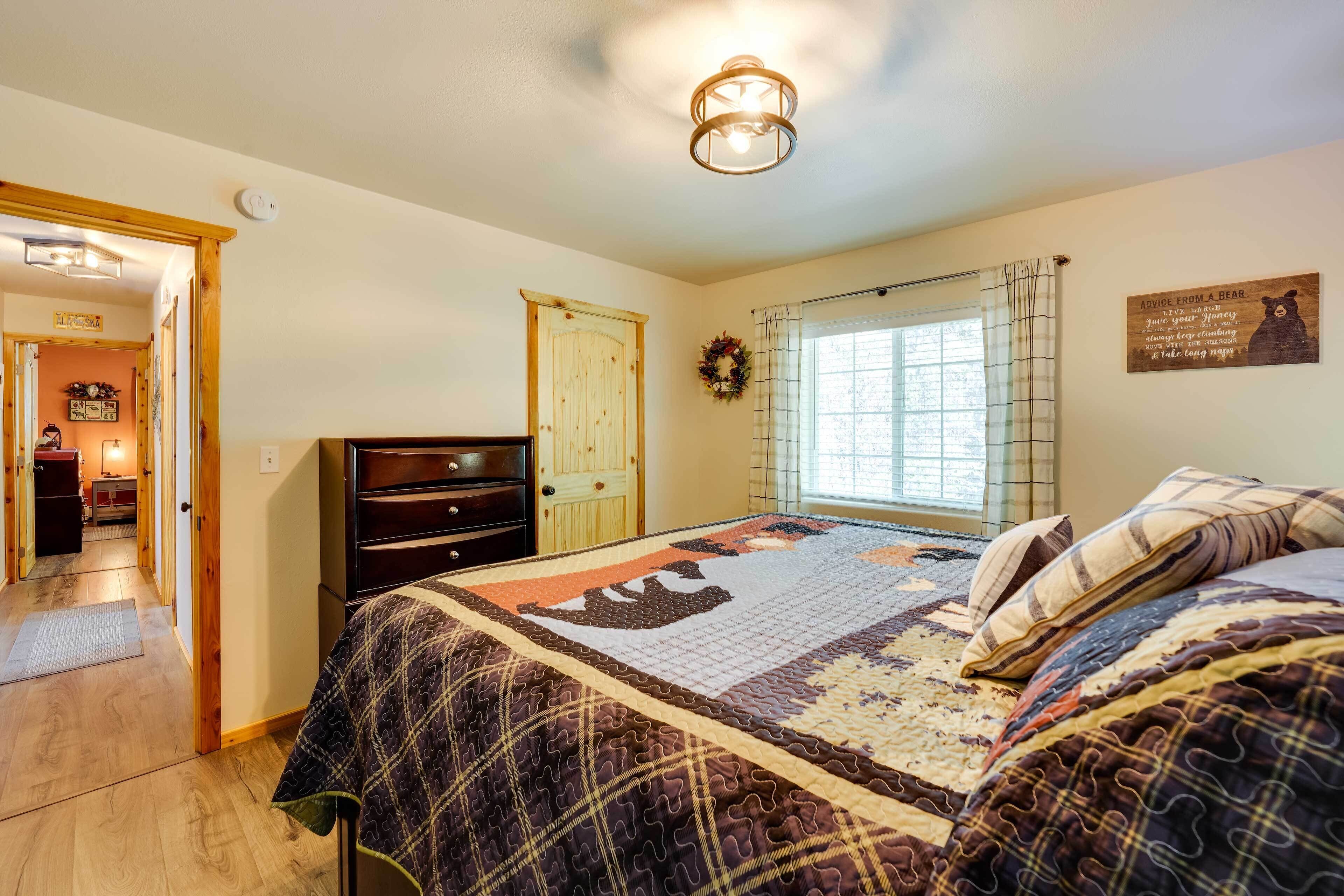 A bedroom with a large bed, a dresser, a window with curtains, and a door.
