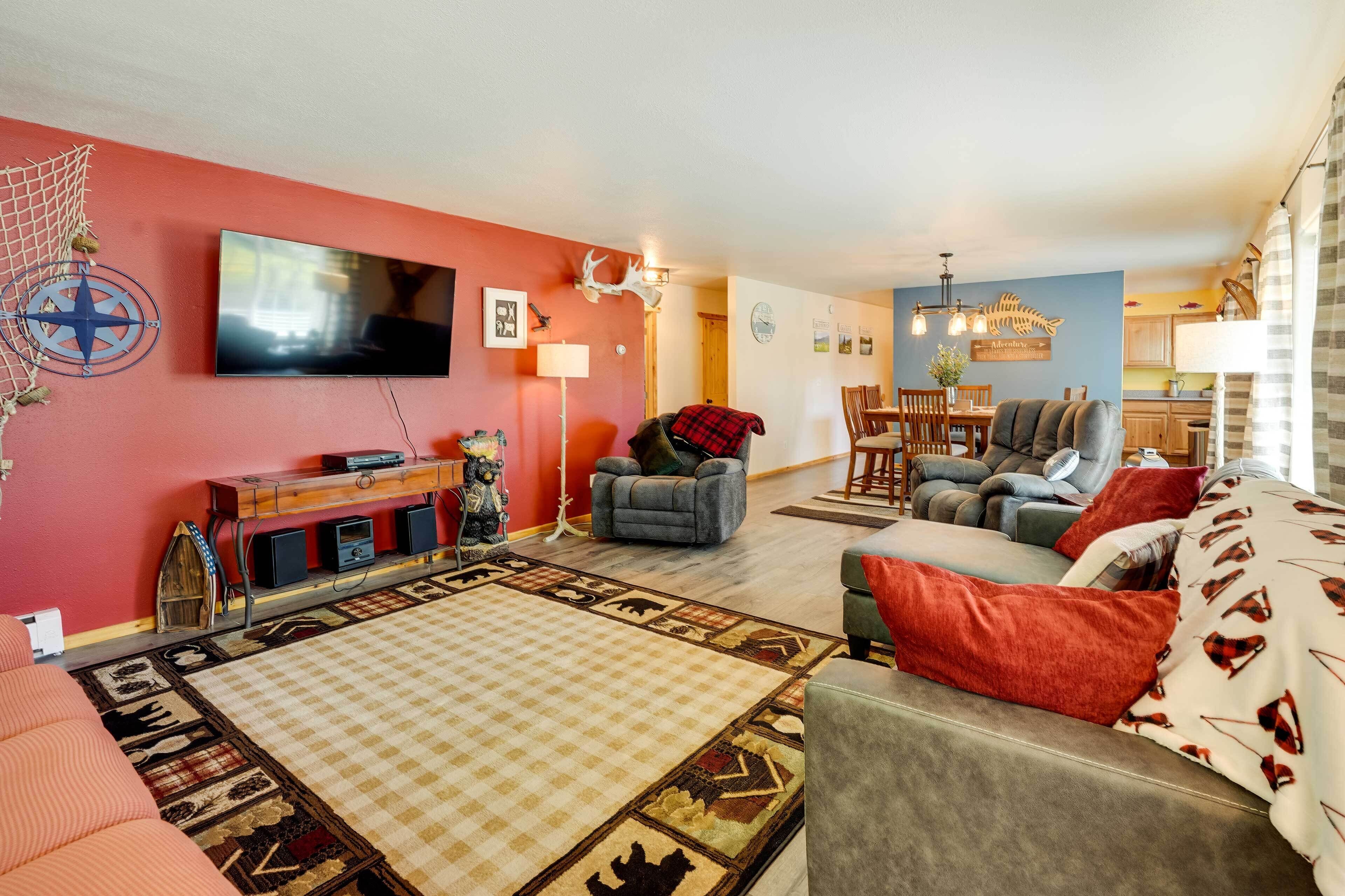 A living room with a red wall, a flat-screen TV, a fireplace, a sofa, and a dining area with wooden furniture.