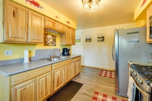 A kitchen with wooden cabinets, a stainless steel refrigerator, a stove, and a coffee maker. - Single-story Soldotna Home Near the Kenai River! (Soldotna)