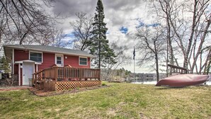 Une maison rouge avec une terrasse en bois et une jetée qui s’avance dans un lac.