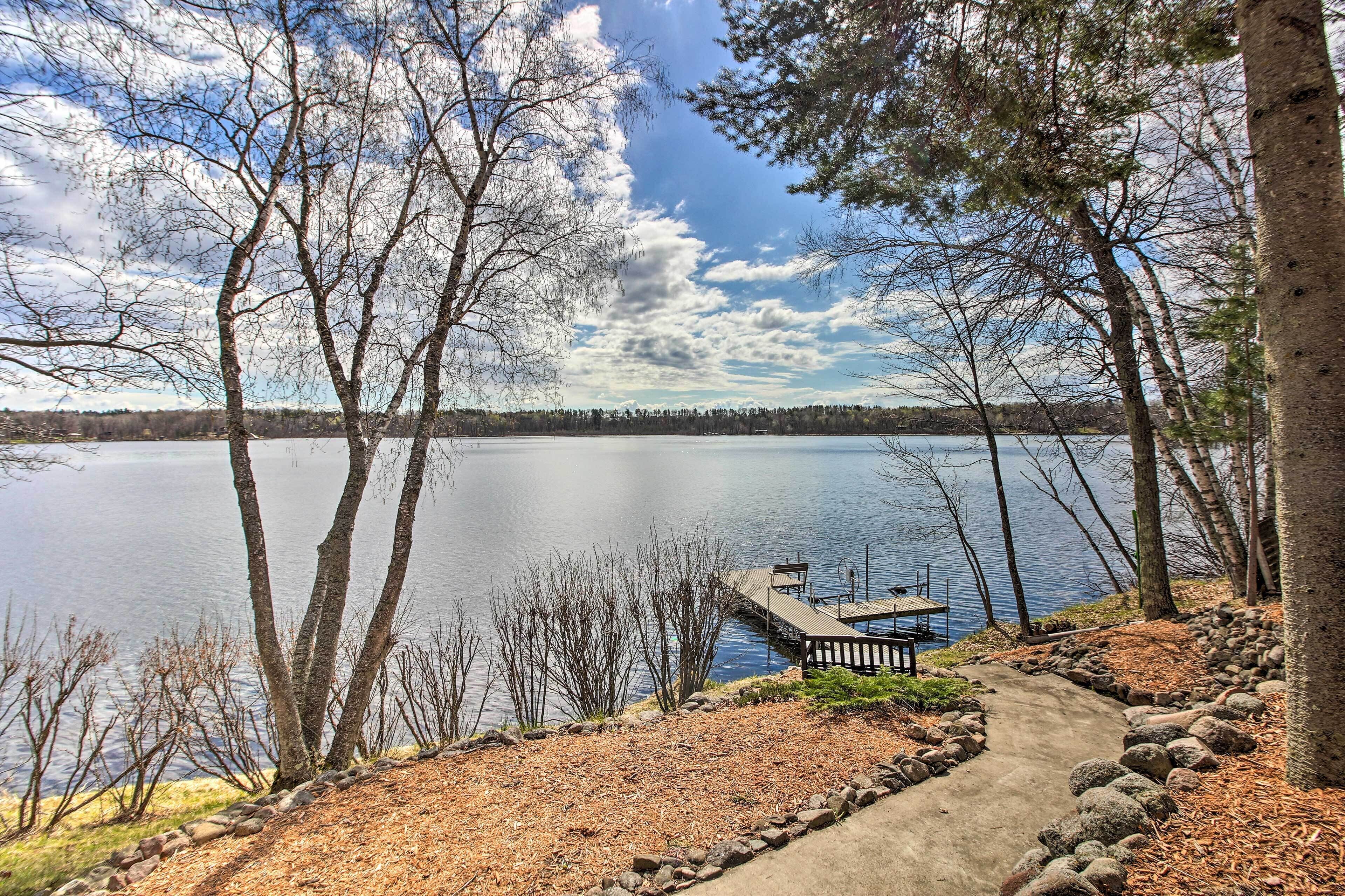 A lakeside view with a dock and a concrete path leading to a wooden deck.
