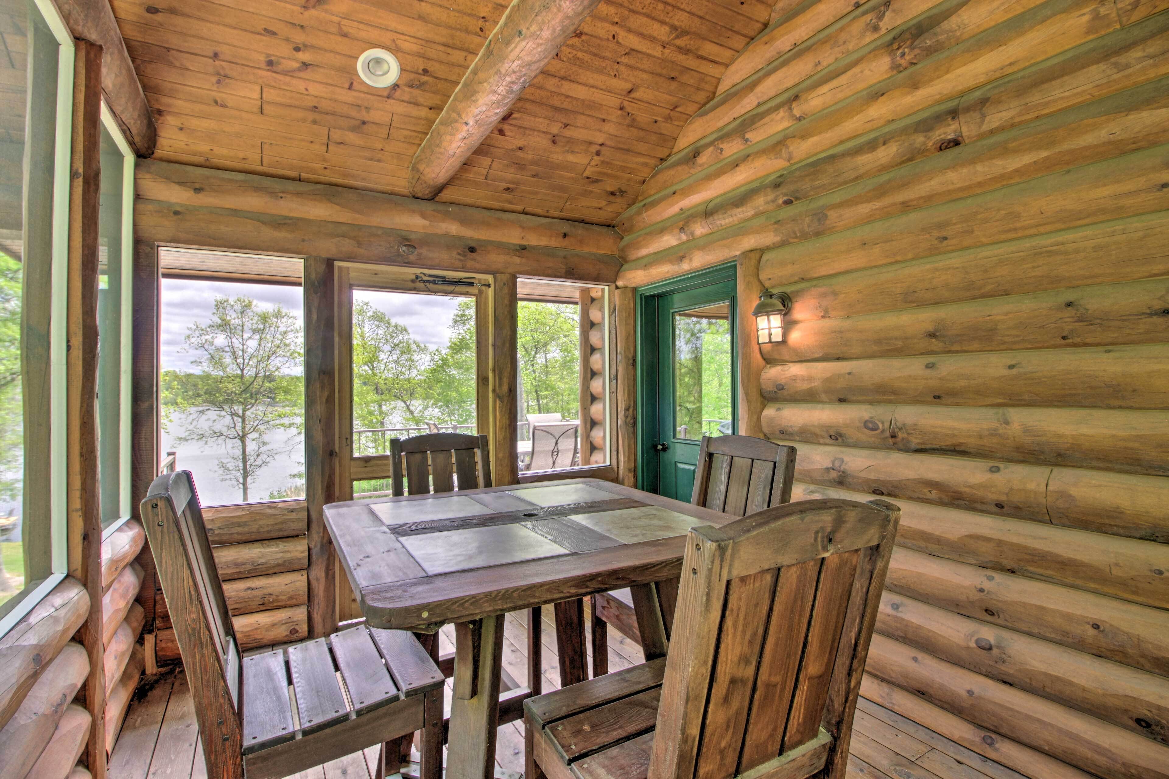 Una cabaña de madera con una mesa de comedor y sillas, ventanas amplias y vistas a árboles.