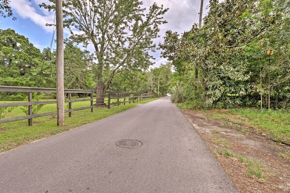 A paved pathway flanked by wooden fences and trees, leading into a natural setting. - Charming Family Cottage Near Pass Christian Beach! (Pass Christian)