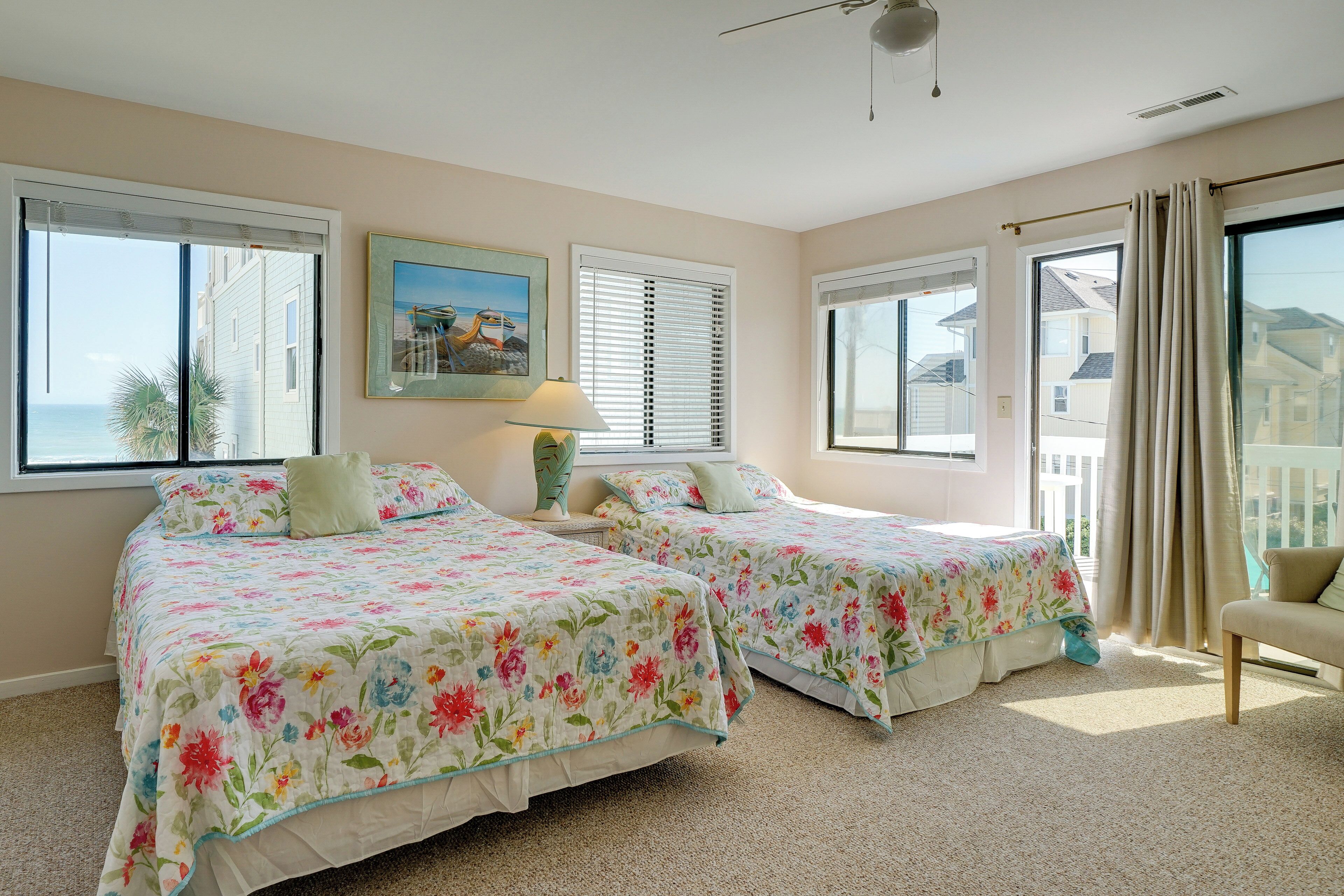 A bedroom with two beds, large windows, a ceiling fan, and a view of the ocean.