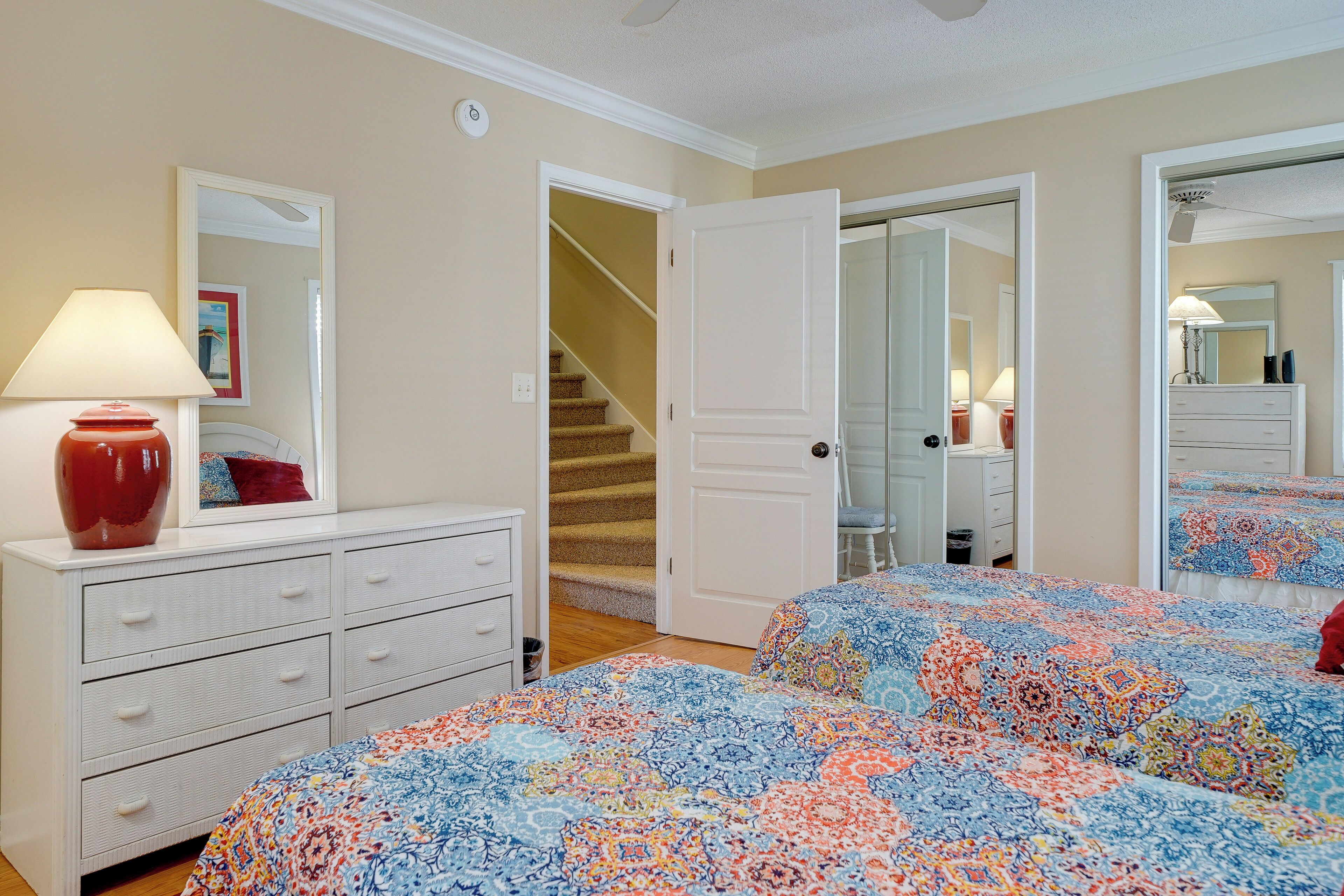 A bedroom with two beds, a dresser, a mirror, and a staircase leading to another room.